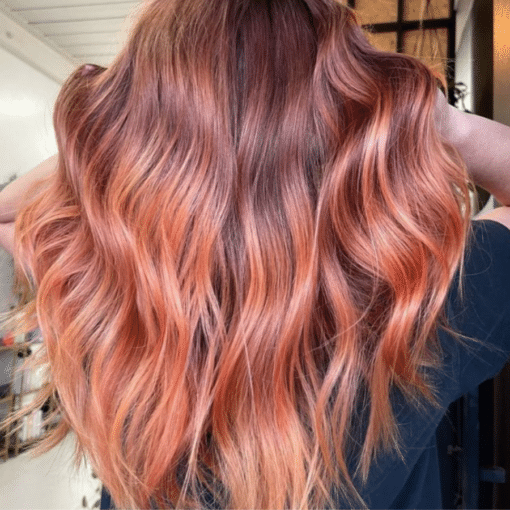 Long, wavy hair with a warm coppery auburn peach ombre colour, toned with Muvo Just Peachy Shampoo 300ml. Shown from behind on a person wearing a dark navy shirt.